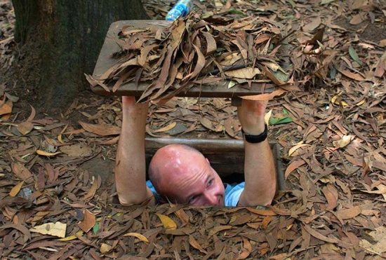 An american tourist is happy with Cu Chi Tunnels.